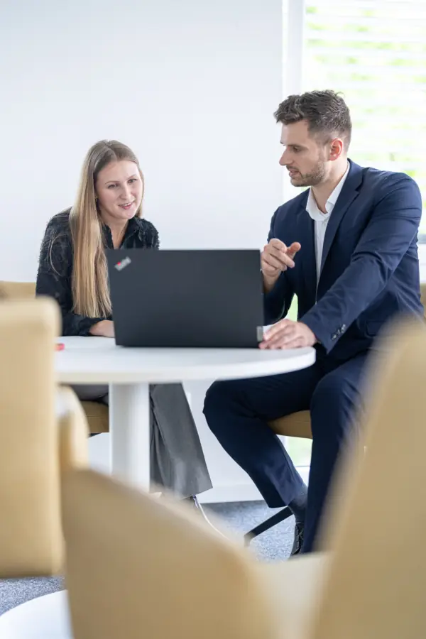 Beraterin und Berater besprechen etwas gemeinsam am Laptop am runden Tisch