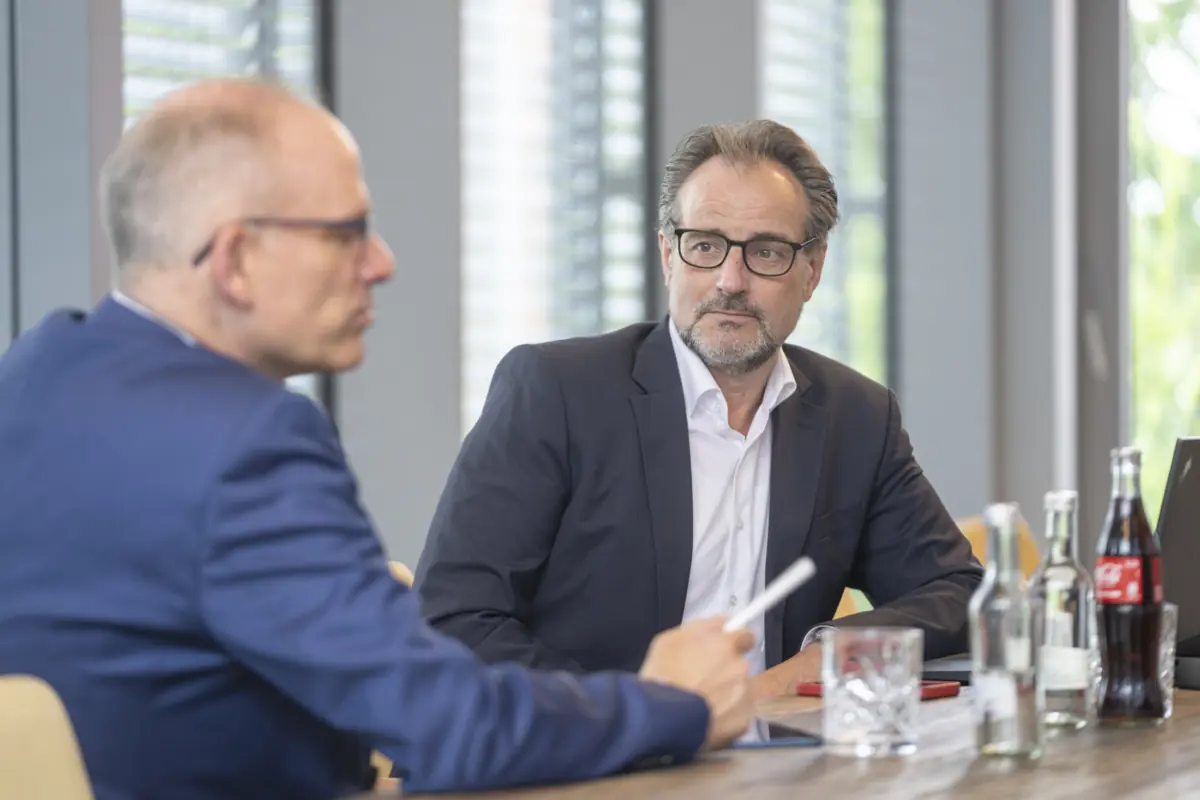Zwei Berater im Gespräch am Besprechungstisch, einer mit Brille und Bart hört aufmerksam zu