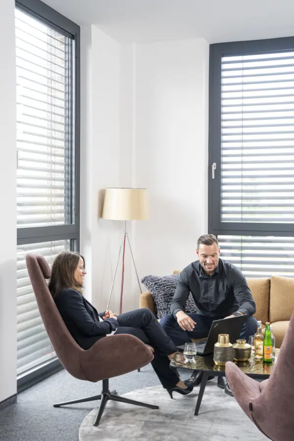 Beraterin und Berater besprechen sich mit Laptop in der Sitzecke eines hellen Büros