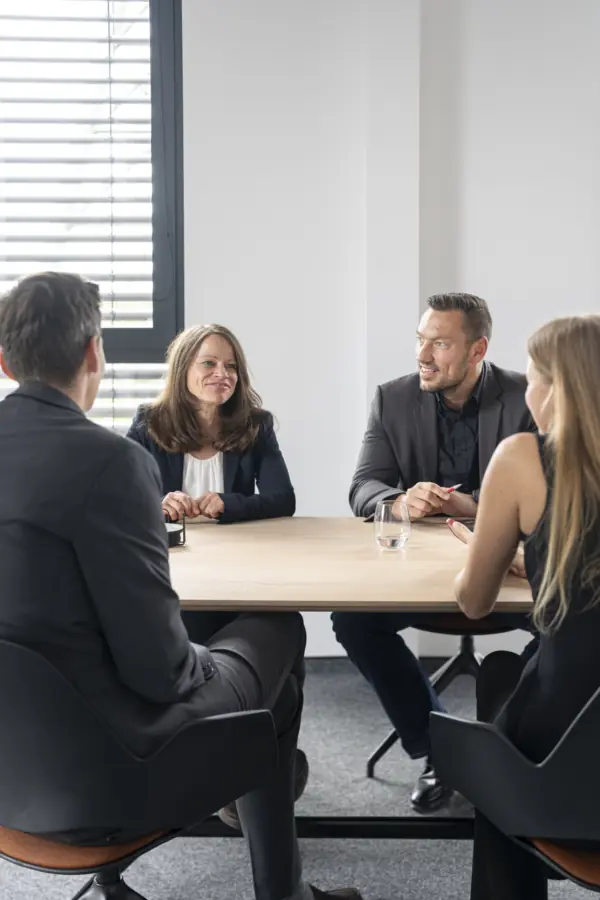 Vier Berater und Beraterinnen im Gespräch an einem runden Besprechungstisch