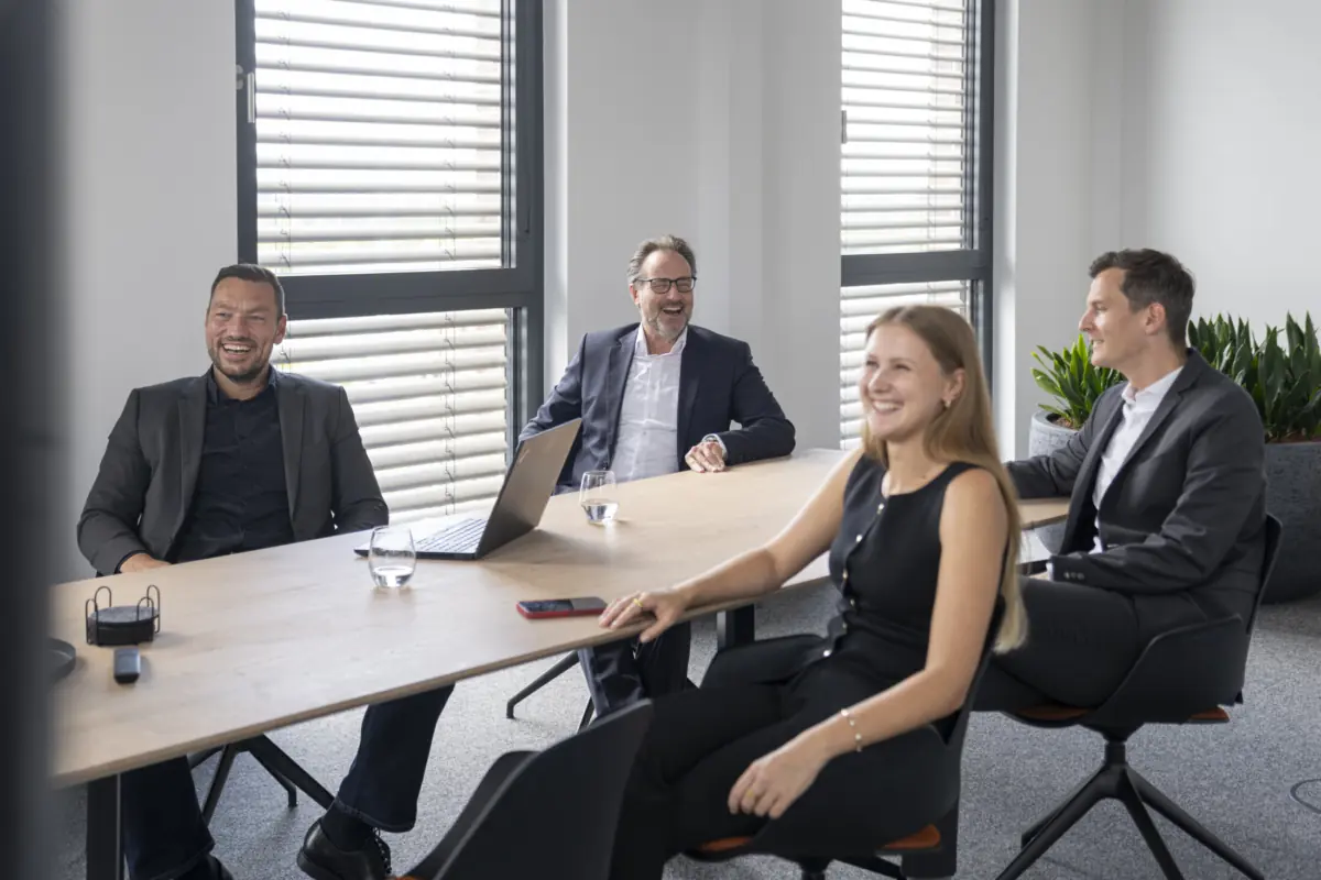 Vier lachende Kolleginnen und Kollegen sitzen entspannt an einem Besprechungstisch im hellen aurantia-Büro